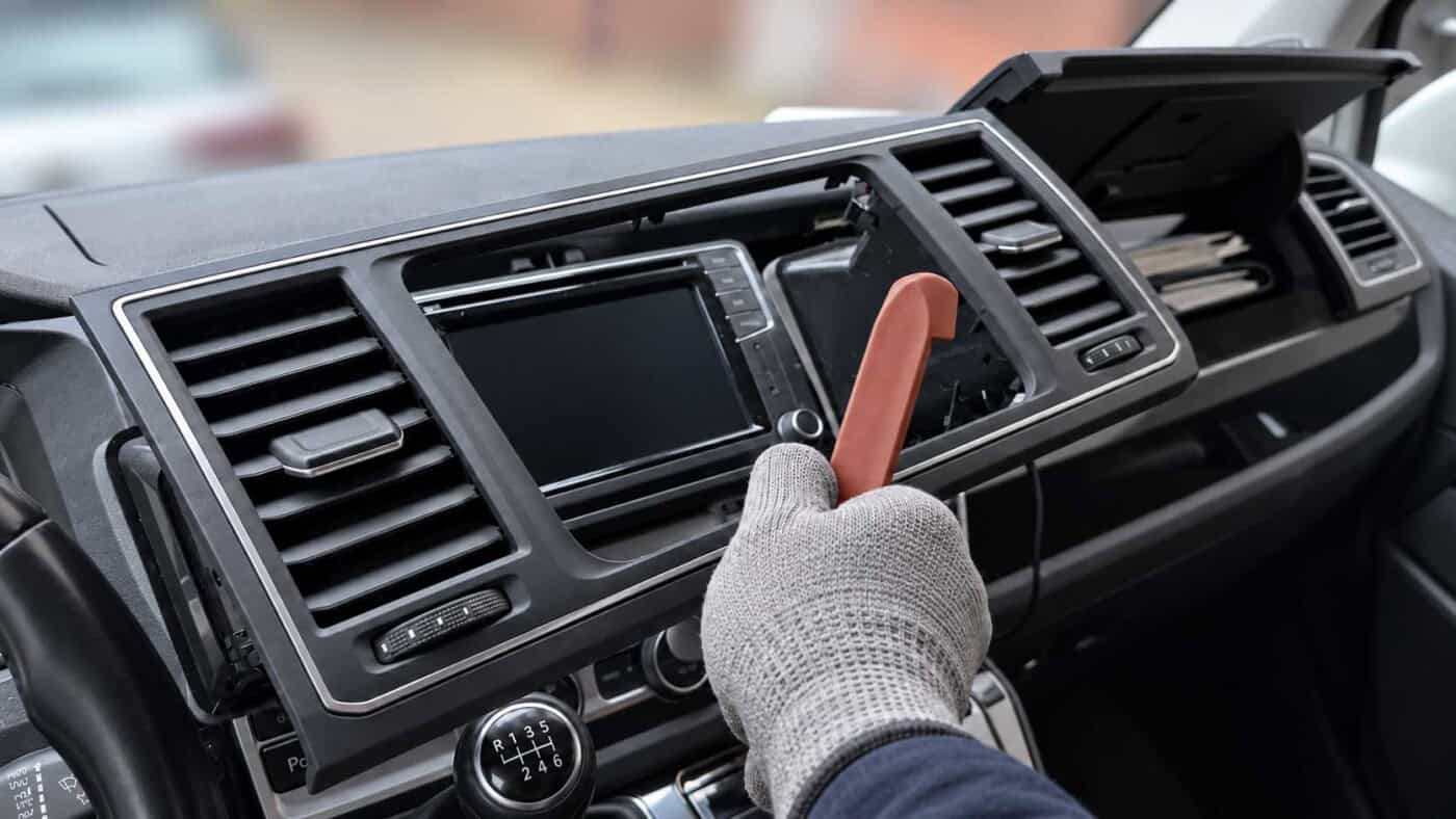 Abgenommener Radiorahmen mit beiden Lüftungsdüsen im VW T6 ab 2015, davor eine Hand mit Kunststoffhebel.